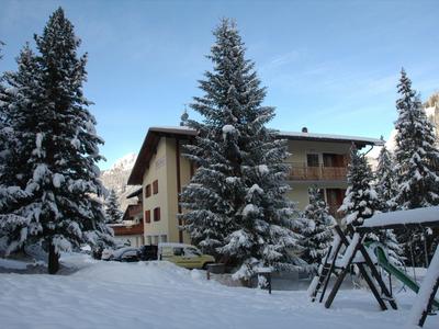 Schneebedecktes Hotelgebäude mit Tannenbäumen und Spielplatz im Winter.