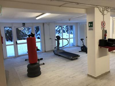 Helles Fitnessstudio mit Laufband, Boxsack und Heimtrainer mit Fenstern zum Schnee draußen.