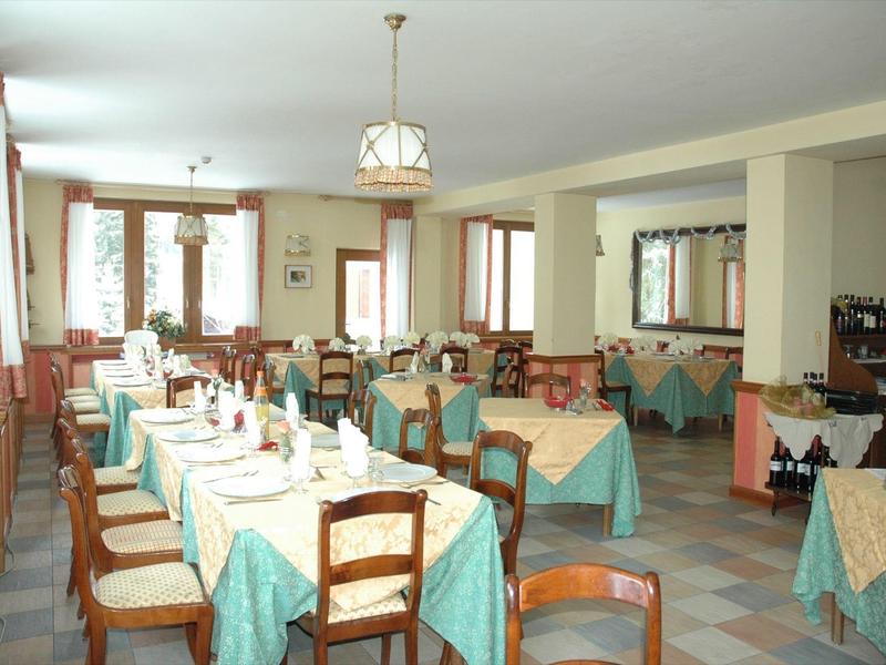 Großer Speisesaal mit blau-grünen Tischdecken, Holztischen und Stühlen, heller Raum mit Fenstern.