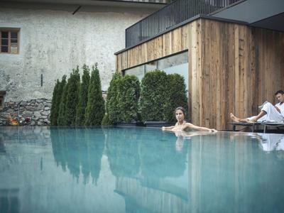 Frau entspannt im Pool eines modernen Hotels mit Mann auf Liegestuhl nebenan.