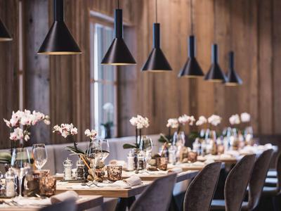 Langer gedeckter Holztisch mit Blumentöpfen, Kerzen und aufgehängten schwarzen Lampen in modernem Raum.