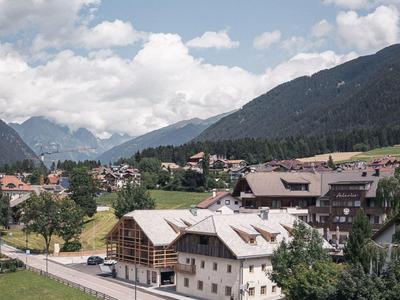 Bergdorf mit Häusern, grünen Wiesen und bewaldeten Hügeln unter blauem Himmel mit Wolken.