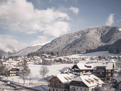 Winterliches Bergdorf mit schneebedeckten Häusern, Bergen und bewölktem Himmel.