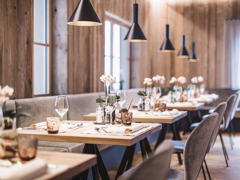 Gemütlicher Gastraum mit Holzwänden, modernen Hängelampen und gedeckten Tischen mit Blumen.