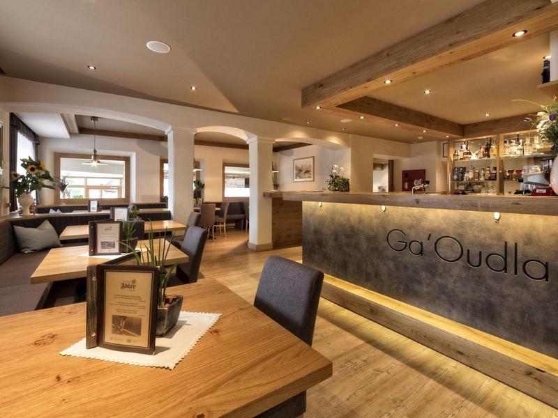 Moderne Cafeteria mit Holztischen, grauen Sitzbänken und beleuchtetem Tresenbereich.