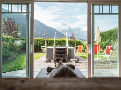 Blick durch eine Glastür auf eine Terrasse mit Sitzmöbeln und Berglandschaft im Hintergrund.