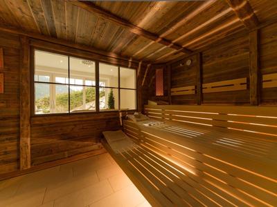 Sauna mit Holzwänden, -bänken und großer Fensterfront, durch die Tageslicht strömt.
