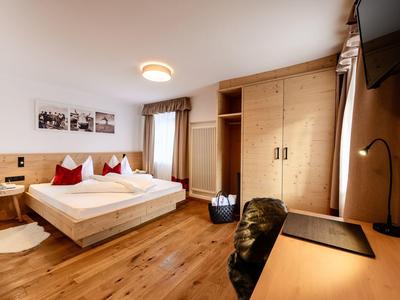 Helles Hotelzimmer mit Doppelbett, Holzboden, großem Kleiderschrank und Schreibtisch mit Fernseher.