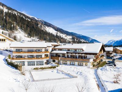 Großes Hotel in verschneiter Berglandschaft mit klar blauem Himmel und bewaldeten Hängen.