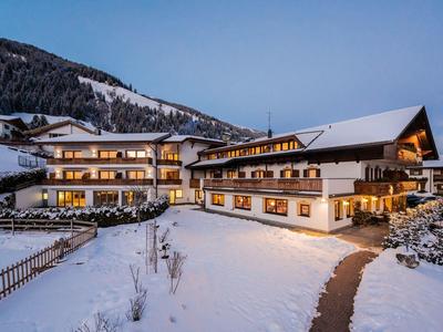 Großes traditionelles Hotel mit Holzfassade im verschneiten Bergdorf bei Abenddämmerung.