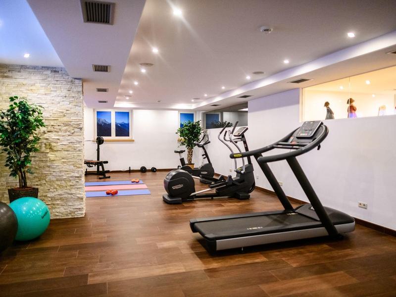 Moderner Fitnessraum mit Laufband, Crosstrainer, Hanteln und grünem Gymnastikball auf Holzboden.