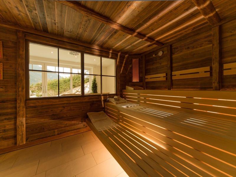Sauna mit Holzwänden, -bänken und großer Fensterfront, durch die Tageslicht strömt.
