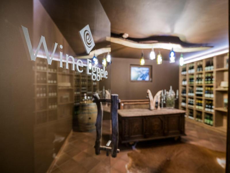 Moderner Weinkeller mit Holzregalen, Theke, Weinfass und dekorativer Beleuchtung.