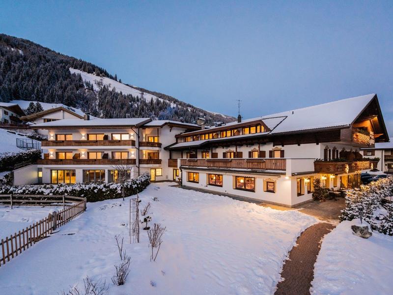 Großes traditionelles Hotel mit Holzfassade im verschneiten Bergdorf bei Abenddämmerung.