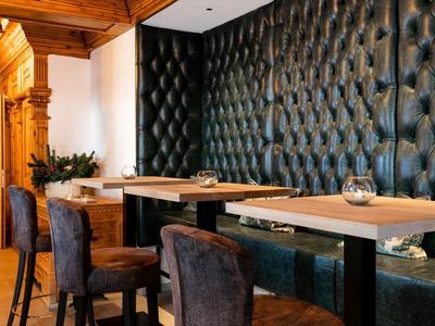 Moderner Gastraum mit schwarzen Polsterstühlen, Holzdecken und gemütlicher Ledersitzbank.