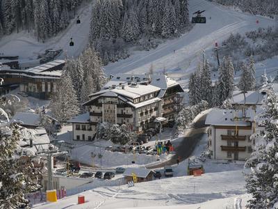 Winterliche Berglandschaft mit schneebedeckten Häusern und Bäumen an einem Skihang.