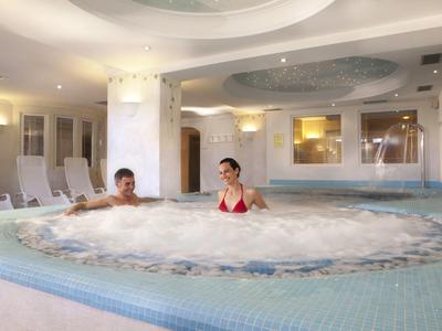 Ein Paar entspannt im sprudelnden Whirlpool eines hellen, modernen Wellnessbereichs.