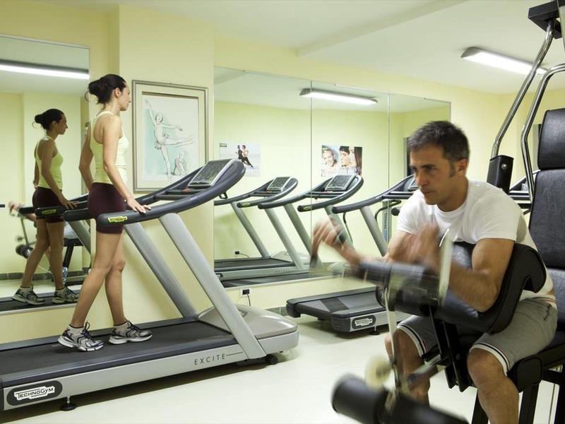 In einem Fitnessraum trainiert eine Frau auf dem Laufband, während ein Mann Übungen an einer Kraftmaschine macht.