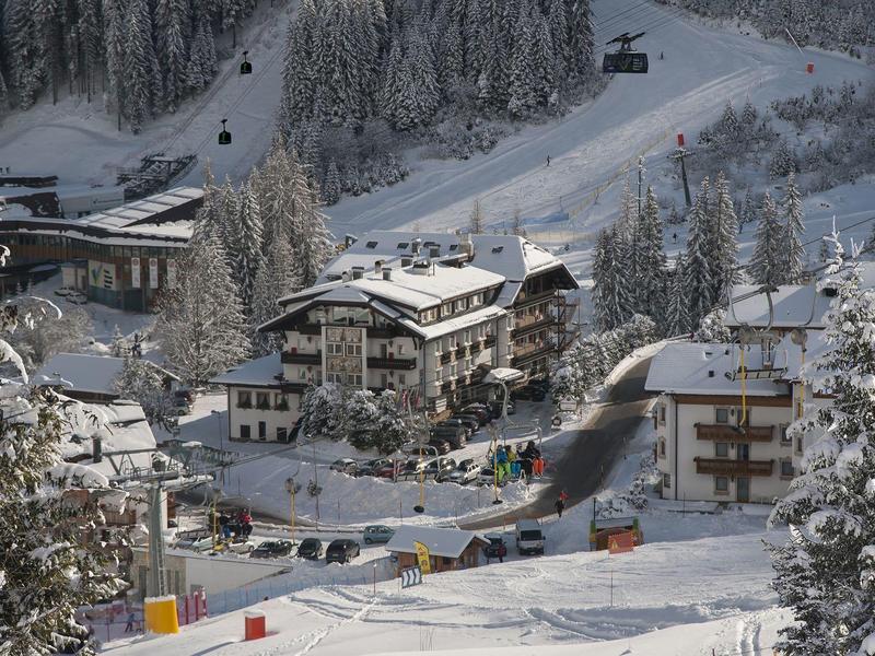 Winterliche Berglandschaft mit schneebedeckten Häusern und Bäumen an einem Skihang.