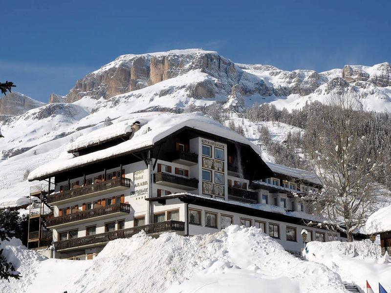 Ein großes Chalet in den verschneiten Alpen vor blauem Himmel und Felsen im Hintergrund.