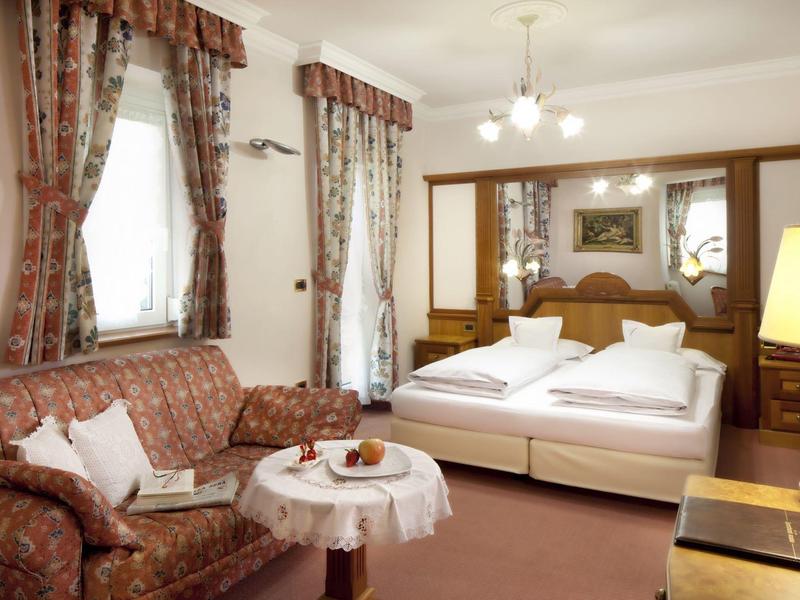 Wohnzimmer mit braunem Sofa, rundem Tisch und angrenzendem Schlafzimmer mit Doppelbett.