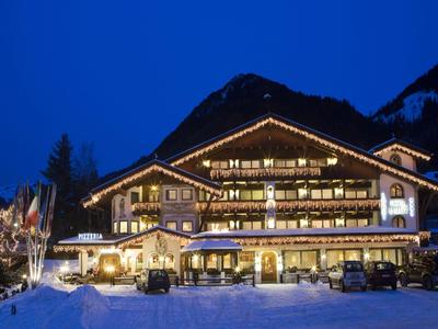 Beleuchtetes Berghotel bei Nacht mit Schnee und Parkplätzen im Vordergrund.