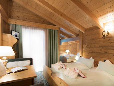 Gemütliches Hotelzimmer mit Holzwänden, Doppelbett und Schreibtisch unter schrägem Dach.