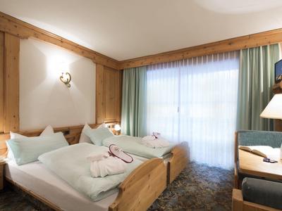 Hell eingerichtetes Hotelzimmer mit zwei Einzelbetten und einem Schreibtisch am Fenster.