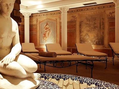 Eleganter Wellnessbereich mit Skulptur, Liegestühlen und Wandmalereien in warmem Licht.
