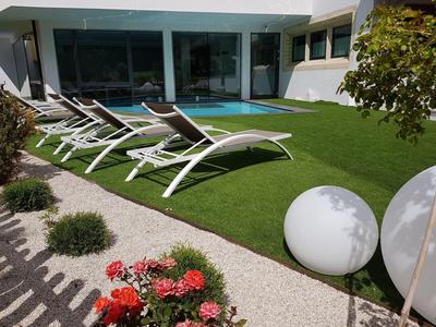 Grüner Garten mit Liegestühlen und Pool vor einem modernen Hotelgebäude.