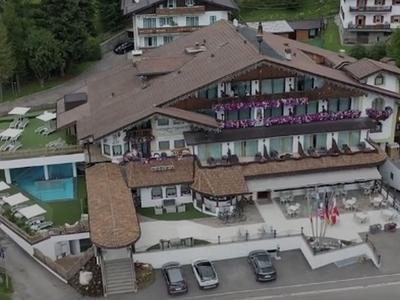 Großes Hotel mit braunem Dach, Balkonblumen, Außenpool und Parkplatz in ländlicher Umgebung.
