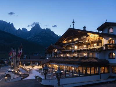 Alpenhotel bei Dämmerung mit beleuchteten Balkonen und Bergkulisse im Hintergrund.