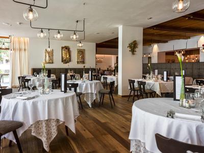 Helles Restaurant mit runden Tischen, weißen Tischdecken und Holzboden. Große Fenster lassen Tageslicht herein.