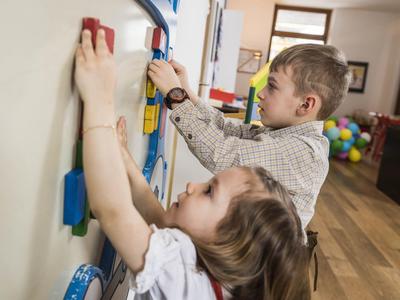 Zwei Kinder stehen an einer weißen Magnettafel und befestigen bunte Magnetformen daran.