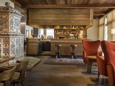 Gemütliche Gaststube mit Holzbalken, buntem Kachelofen, roten Sesseln und Holztischen.