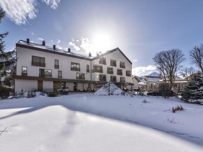 Großes weißes Haus im Winter mit verschneitem Garten und strahlend blauem Himmel im Hintergrund.