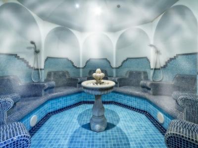 Rundes türkisches Bad mit blauen Fliesen, Nischenbänken und einem Brunnen in der Mitte.