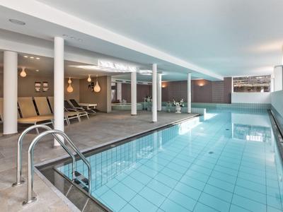 Moderner Indoor-Pool mit blauer Fliesen, weißen Säulen und Liegestühlen an einer Wand.
