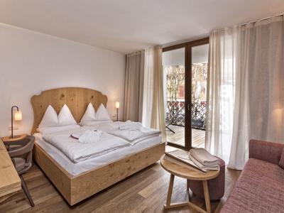 Gemütliches Schlafzimmer mit Holzbetten, Balkon, Schreibtisch, Sofa und warmem Licht.