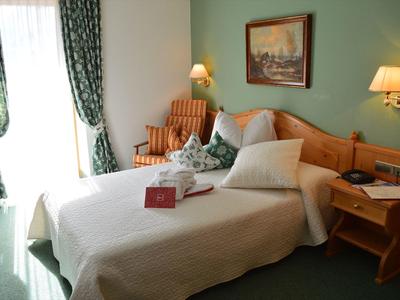 Gemütliches Schlafzimmer mit Doppelbett, Holzmöbeln, grünem Teppich und vorgezogenen Vorhängen.