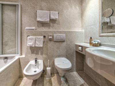 Modernes Badezimmer mit Badewanne, Bidet, Toilette, großem Spiegel und weißen Handtüchern an der Wand.