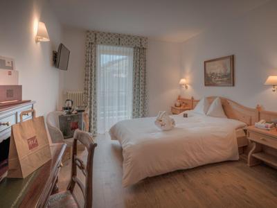 Gemütliches Hotelzimmer mit Doppelbett, Holzmöbeln und Balkonblick.