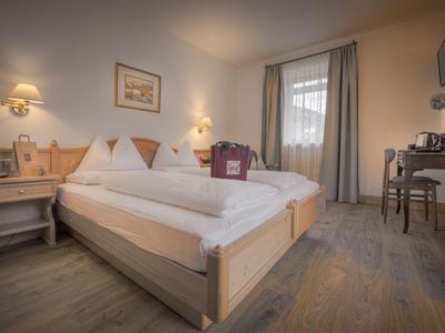 Gemütliches Hotelzimmer mit Doppelbett, Beistelltischen, Schreibtisch und großen Fenstern mit Vorhängen.