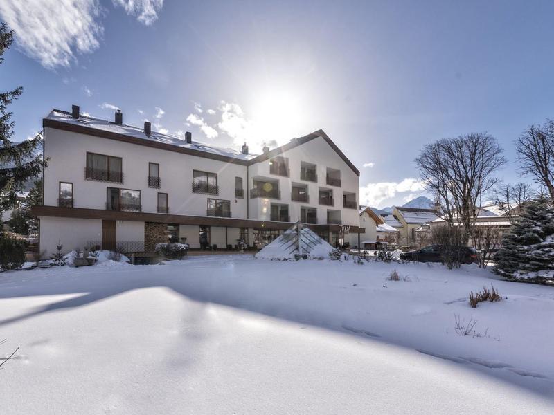 Großes weißes Haus im Winter mit verschneitem Garten und strahlend blauem Himmel im Hintergrund.