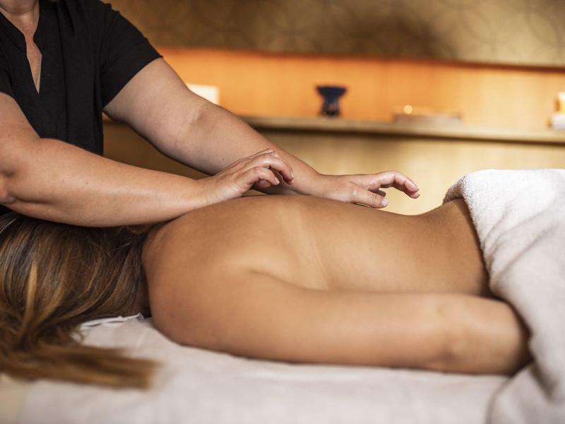 Frau liegt entspannt auf Massagetisch, während Hände Rücken und Schultern massieren.