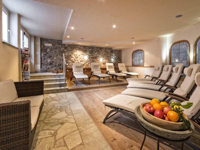 Ruheraum mit Liegestühlen, Steinwand, gedämpftem Licht und Obstteller auf kleinem Tisch.