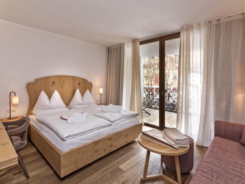 Gemütliches Schlafzimmer mit Holzbetten, Balkon, Schreibtisch, Sofa und warmem Licht.