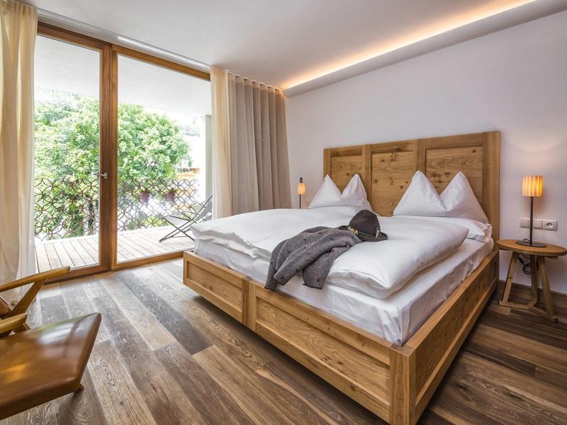 Modernes Schlafzimmer mit Holzmöbeln, großem Bett, bodentiefen Fenstern und warmem Licht.