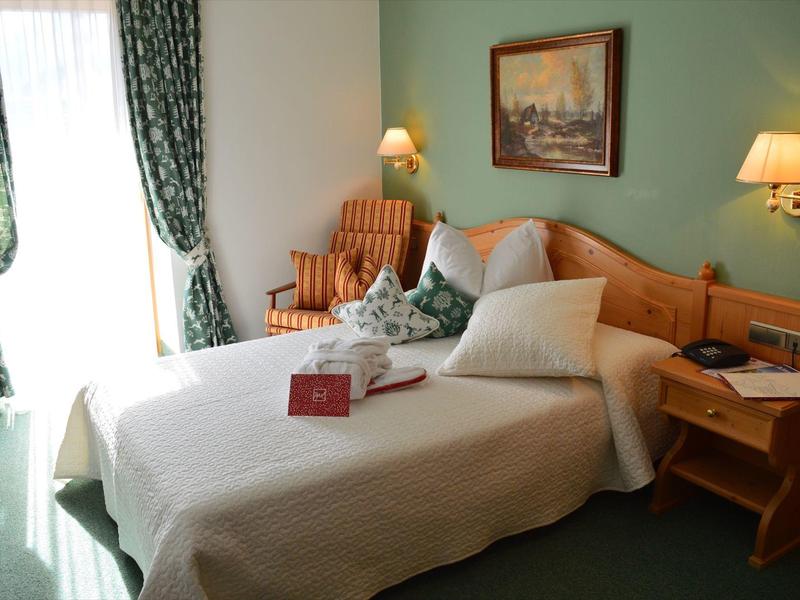 Gemütliches Schlafzimmer mit Doppelbett, Holzmöbeln, grünem Teppich und vorgezogenen Vorhängen.