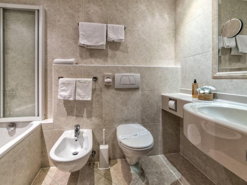 Modernes Badezimmer mit Badewanne, Bidet, Toilette, großem Spiegel und weißen Handtüchern an der Wand.